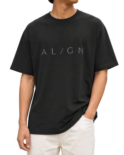 Young male model wearing a black oversized T-shirt with a minimalist “AL/GN” typography design across the chest.