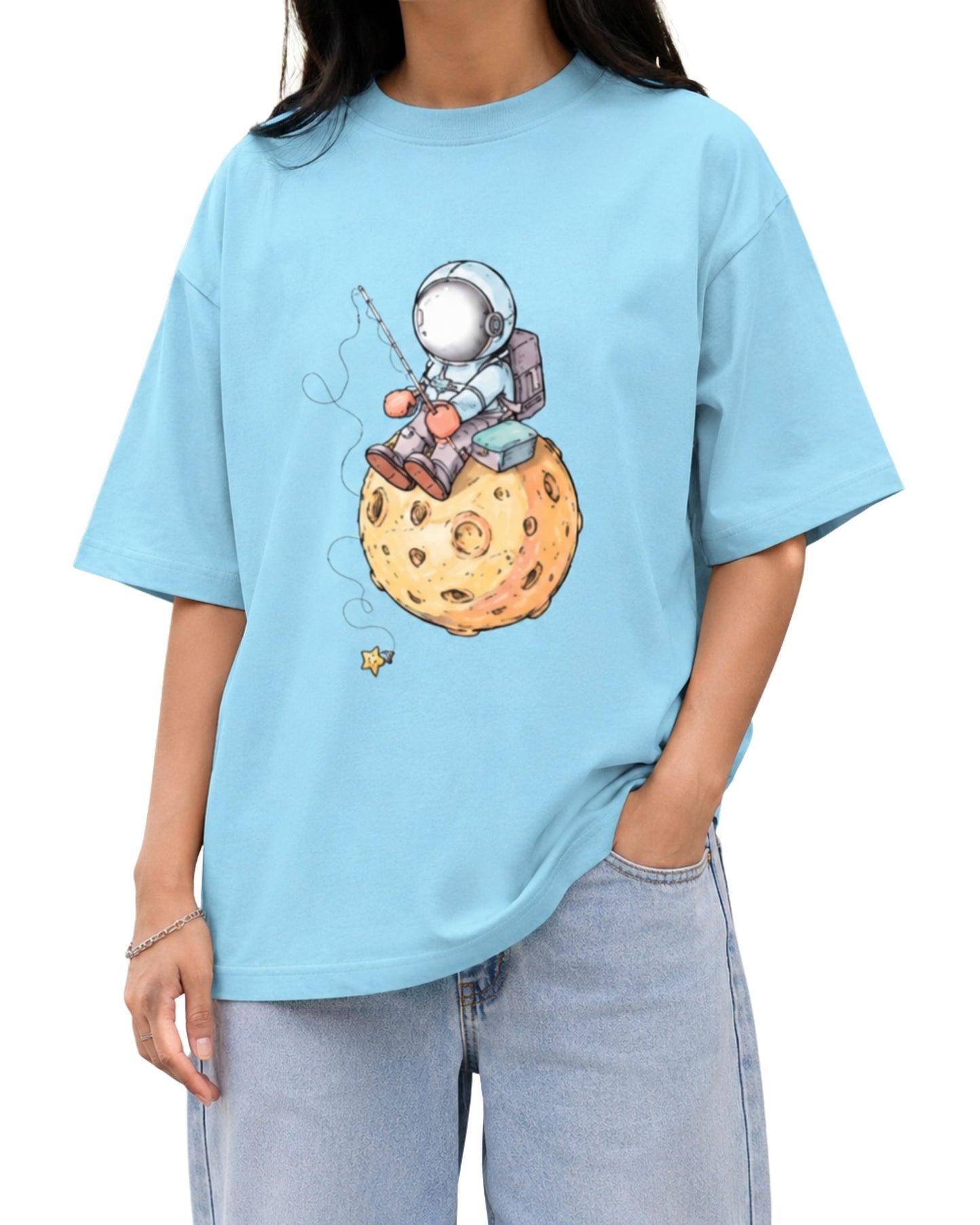baby blue graphic T-shirt featuring a whimsical astronaut sitting on a cratered moon while holding a fishing rod, illustrated in a playful hand-drawn space-themed style.