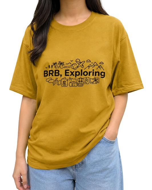 Mustard yellow graphic T-shirt with bold “BRB, Exploring” text, surrounded by playful travel-inspired doodles including mountains, palm trees, an airplane, luggage, camera, map, and location icons.