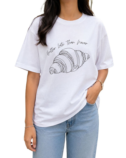 Minimal line-art croissant illustration with the handwritten phrase “Butter Late Than Never” curved above it white