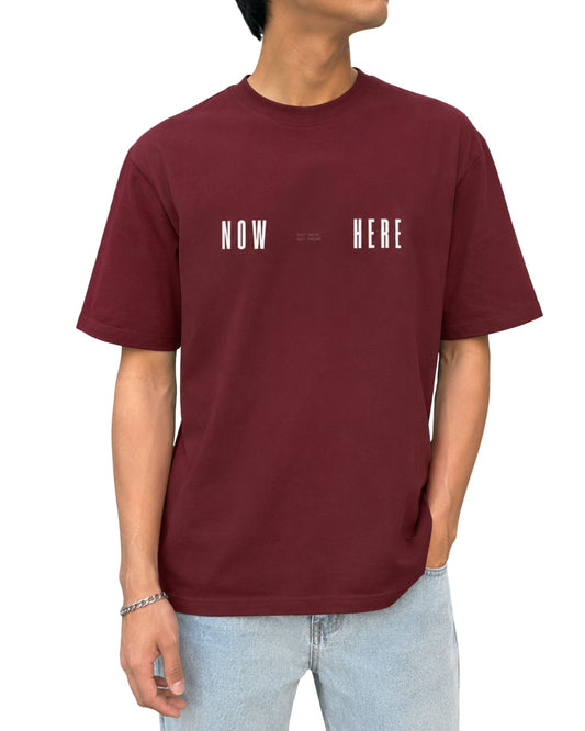 Brick red unisex graphic T-shirt design with bold NOW HERE typography and minimalist NOT HERE NOT THERE text.