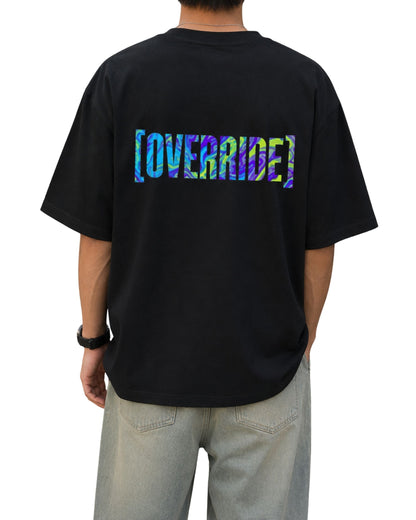 Black oversized T-shirt with a large multicolor glitch-style “OVERRIDE” graphic printed across the upper back.