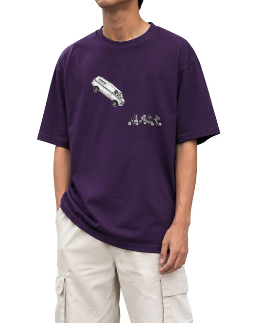 Purple oversized graphic T-shirt featuring a flying van illustration above a row of cyclists in a playful adventure-inspired design.