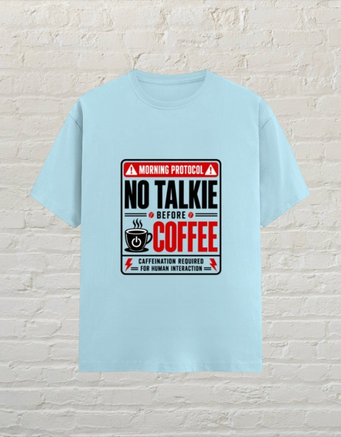 CoreTeez baby blue unisex cotton t-shirt with No Talkie Before Coffee graphic print against a white brick wall