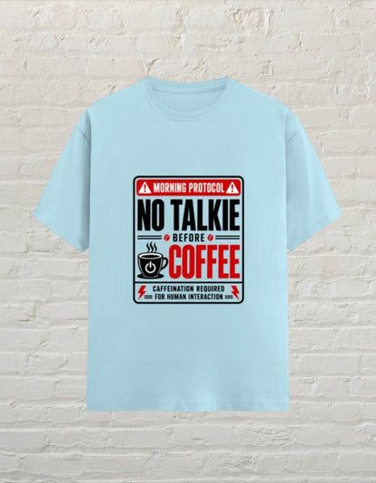CoreTeez baby blue unisex cotton t-shirt with No Talkie Before Coffee graphic print against a white brick wall