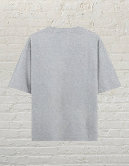 CoreTeez grey unisex oversized cotton t-shirt, back view against a white brick wall background.