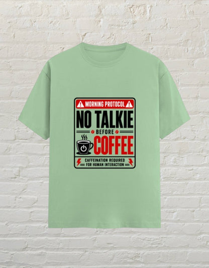 CoreTeez unisex jade cotton t-shirt featuring a No Talkie Before Coffee graphic print on a brick background.