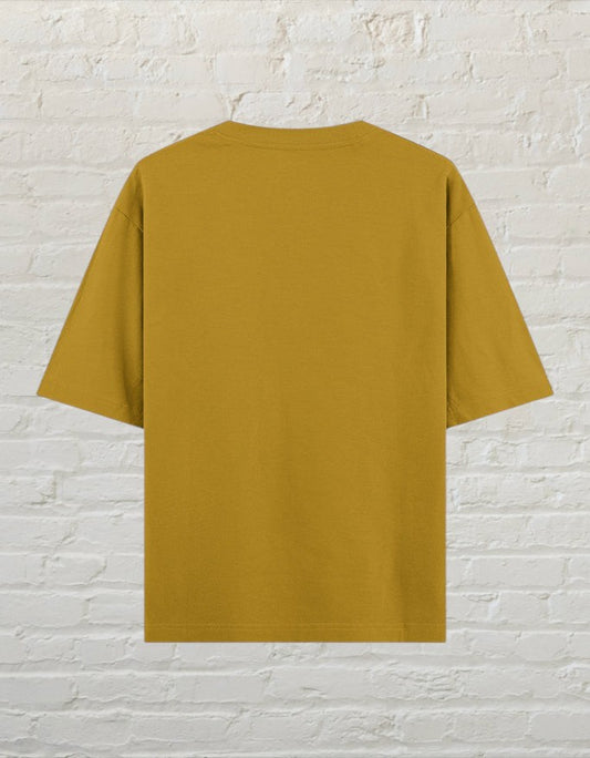 Back view of a mustard yellow CoreTeez unisex oversized cotton t-shirt against a white brick wall background.