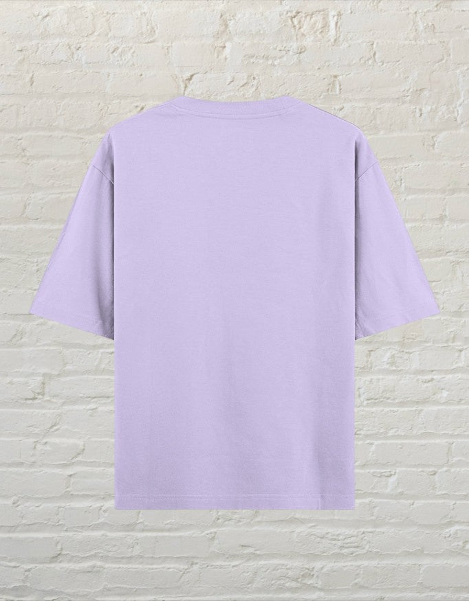 CoreTeez unisex oversized cotton t-shirt in light purple, back view against a white brick wall background.